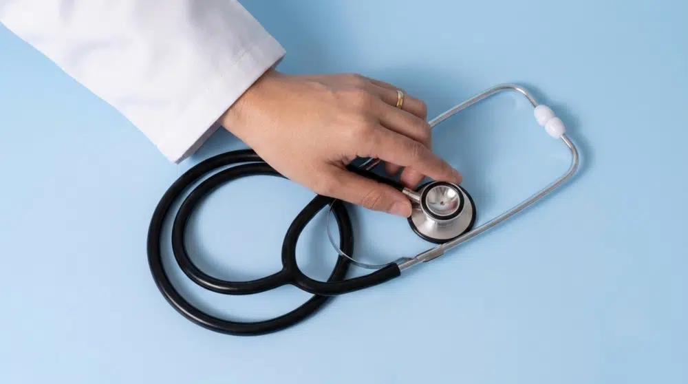 Main d'un médecin tenant un stéthoscope sur fond bleu